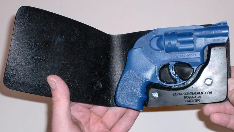 May include: A black leather wallet with a blue handgun holster. The blue handgun is partially visible, with the text "RUGER LCR" and "KEVINSCONCEALMENT.COM" on the holster. The wallet is held open, showcasing the holster's design.