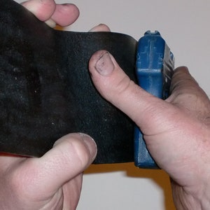 May include: A black leather wallet being held open with a blue and black tool in the right hand.
