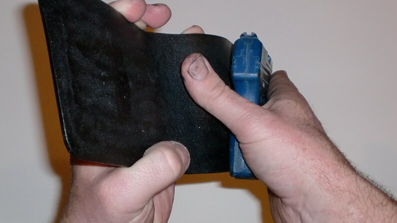 May include: A black leather wallet being held open with a blue and black tool in the right hand.