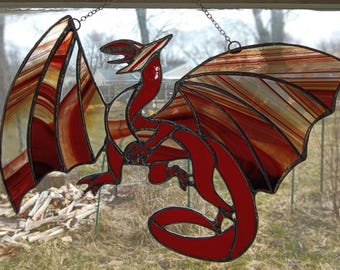 May include: A stained glass dragon with red, white, and brown wings. The dragon is hanging from a chain.
