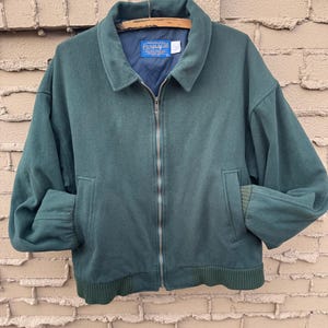 May include: A dark teal wool jacket with a full zipper closure, two front pockets, and a ribbed hem and cuffs. The jacket has a collared neckline and a blue interior lining. The brand name "Pendleton" is visible on a tag inside the jacket.