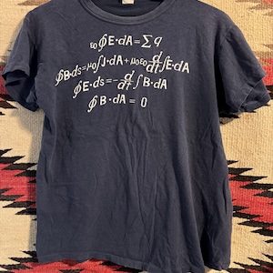 May include: Dark blue t-shirt featuring white mathematical formulas. The equations include integral and differential calculus symbols. The shirt is suspended on a wooden hanger with the text "MAJOR CLEANING SERVICE".