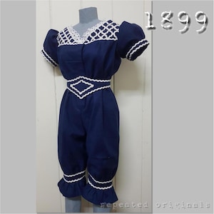 Puede incluir: Un traje de baño de una pieza azul marino con ribete de encaje blanco. El traje de baño tiene un diseño en forma de diamante en la cintura y un dobladillo con volantes.