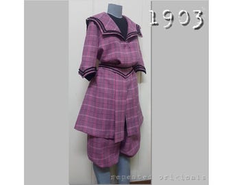May include: A pink and black plaid sailor suit with a black collar and a black belt. The suit is from 1903.