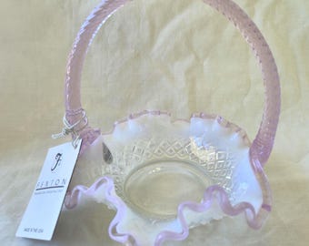 May include: A Fenton glass basket with a ruffled rim and a woven handle. The basket is a pale pink color with a clear, diamond-patterned interior. The tag reads "Fenton" and "Made in the USA."