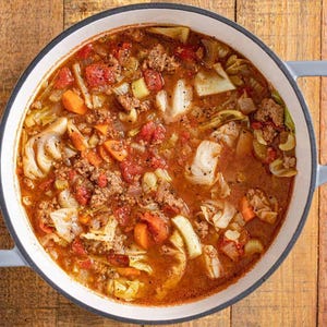 Puede incluir: Una olla blanca llena de una abundante sopa de col con carne picada, zanahorias y tomates.