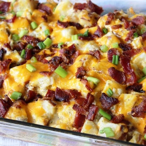 May include: A casserole dish filled with a cheesy potato dish topped with crispy bacon and green onions.