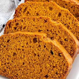 May include: Close-up of several slices of pumpkin bread on a white rectangular plate. The bread is a deep orange color and has a slightly crumbly texture.