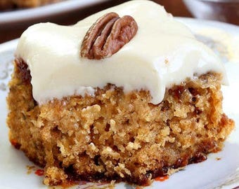 May include: A close-up of a frosted cake with a pecan on top. The cake is a light brown color and has a crumbly texture. The frosting is white and smooth.