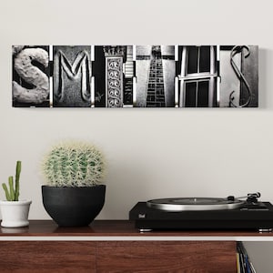May include: Black and white wall art featuring the word "SMITH" spelled out using different architectural details. The art is displayed on a wall above a record player and a wooden shelf.