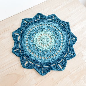 以下が含まれることがあります： 円形のデザインと波状の縁を持つ、ターコイズブルーのクロシェのドイリーです。