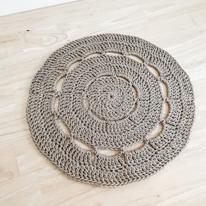 May include: A round, beige crocheted rug with a circular pattern. The rug has a textured surface and a delicate, intricate design.