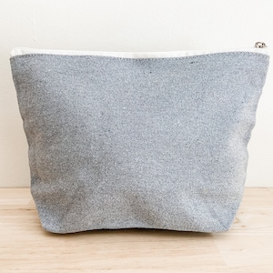 May include: A gray canvas zippered pouch with a white trim. The pouch is made of a soft, textured fabric.