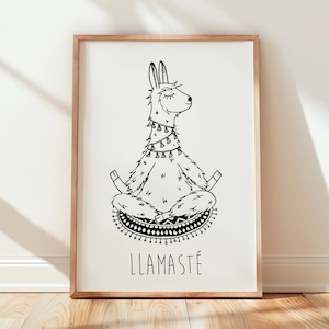 Op de afbeelding: Een ingelijste kunstdruk met een zwart-wit illustratie van een lama in een yogahouding. De lama zit in kleermakerszit, ogen gesloten, met het woord "LLAMASTÉ" eronder. De lijst is lichtbruin.