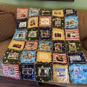 May include: A patchwork quilt with a variety of photos of people and places. The quilt is made of different fabrics, including red, white, and blue, and has a fringed edge. The quilt is a great way to remember loved ones and special moments.
