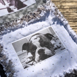 May include: A white quilt with a black and white photo of a dog on it. The quilt has a white background with small black dots and a gray frayed border.
