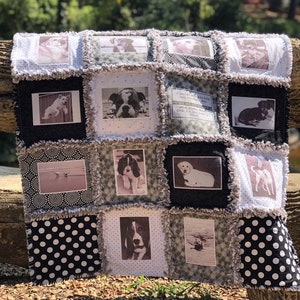 May include: A black and white quilt with a patchwork design featuring photos of dogs. The quilt has a frayed edge and is made of cotton fabric. The quilt is sitting on a wooden bench.