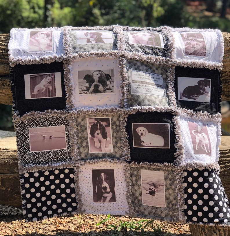 May include: A black and white quilt with a patchwork design featuring photos of dogs. The quilt has a frayed edge and is made of cotton fabric. The quilt is sitting on a wooden bench.