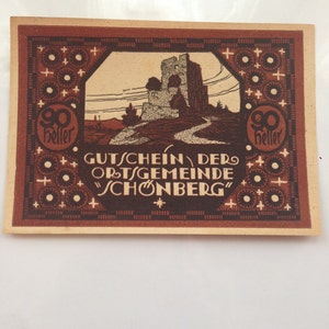 May include: A vintage voucher for 90 heller, featuring a brown and white illustration of a castle with a path leading to it. The voucher is for the Ortsgemeinde Schonberg.