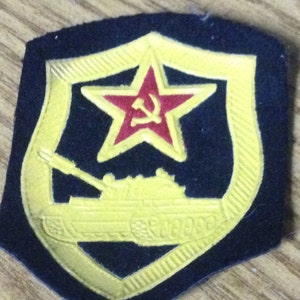 Może przedstawiać: Naszywka wojskowa w kolorze niebieskim i żółtym z czerwoną gwiazdą i sierpem i młotem w środku. Gwiazda jest otoczona żółtą obwódką. Żółty czołg znajduje się pod gwiazdą.