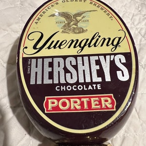 May include: A brown and gold beer tap handle with the text "America's Oldest Brewery" and "Yuengling Hershey's Chocolate Porter" on it.