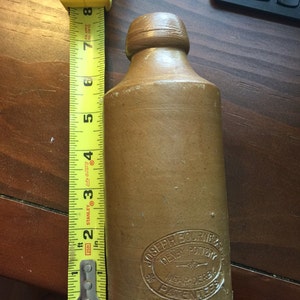 Puede incluir: Una botella de gres marrón con la parte superior redondeada y una etiqueta que dice "Joseph Boupner, Denby Pottery, Near Derby, Patentee".