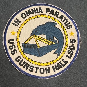 Może przedstawiać: Naszywka haftowana w kolorze niebieskim i żółtym z tekstem "USS Gunston Hall LSD-5" i "In Omnia Paratus" wokół delfina niosącego statek.