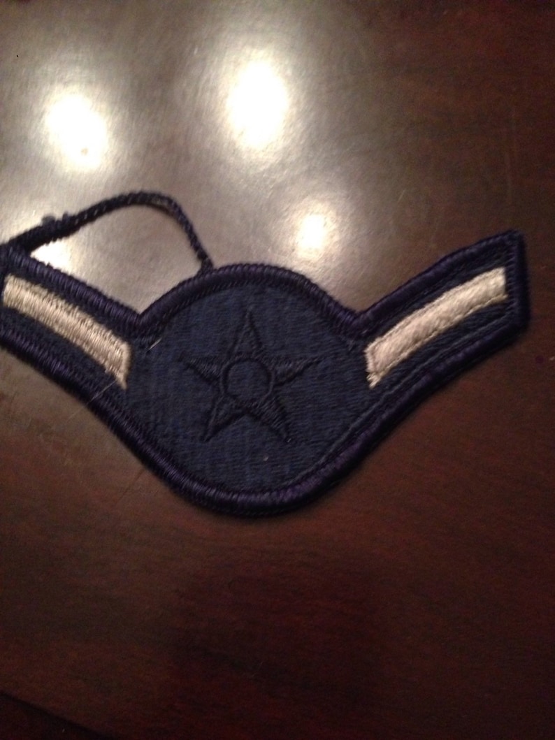 Op de afbeelding: Een blauw en wit militair ranginsigne met een enkele ster in het midden. Het insigne heeft twee witte strepen aan de onderkant.