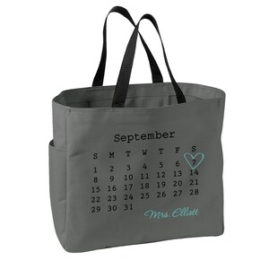 May include: A gray tote bag with black handles featuring a printed September calendar. The number 7 is circled with a light blue heart, and the text Mrs. Elliott is printed in light blue script below the calendar dates on the front of the bag.
