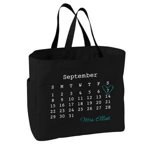 May include: A black tote bag featuring a white printed calendar for the month of September. The number 7 is highlighted with a teal heart outline. Below the calendar, the text Mrs. Elliott is printed in a teal cursive script font.