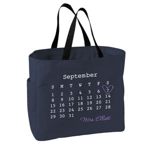 May include: A navy blue tote bag with black handles featuring a white printed September calendar. The number 7 is circled with a light purple heart, and the name Mrs. Elliott is printed in light purple script below the calendar dates.