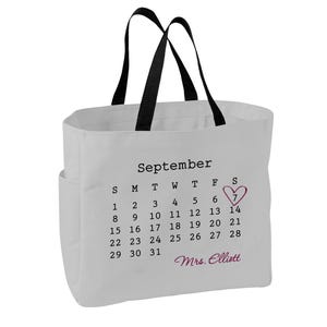 May include: A white canvas tote bag with black handles featuring a printed September calendar. The number 7 is circled with a pink heart, and the name Mrs. Elliott is printed in pink script below the calendar dates on the front of the bag.