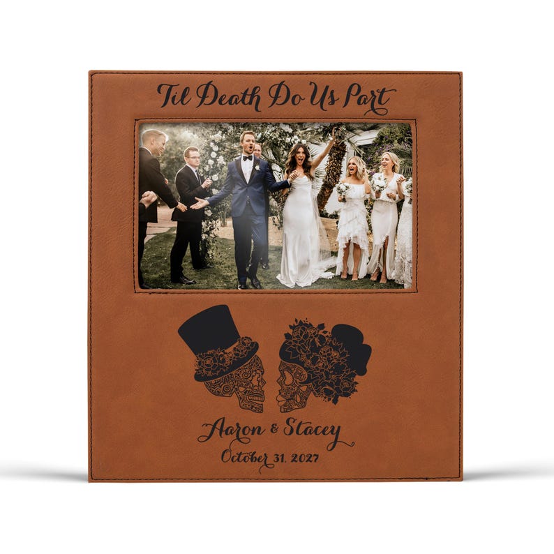 Op de afbeelding: Een bruin lederen fotolijst met een trouwfoto. De lijst is voorzien van de tekst "Til Death Do Us Part" en heeft suikerschedelontwerpen. De namen "Aaron & Stacey" en de datum "October 31, 2027" zijn ook opgenomen.