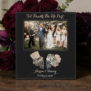 Op de afbeelding: Zwarte fotolijst met een trouwfoto, de tekst "Til Death Do Us Part" en de namen "Aaron & Stacey" met de datum "31 oktober 2027". De lijst heeft decoratieve schedelontwerpen.