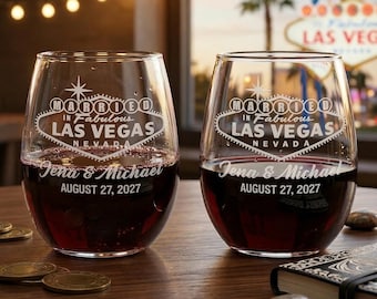 May include: Two stemless wine glasses filled with red wine. Each glass is etched with the words "Married in Fabulous Las Vegas, Nevada" and the names "Jena & Michael" with the date "August 27, 2027". The glasses sit on a wooden surface.
