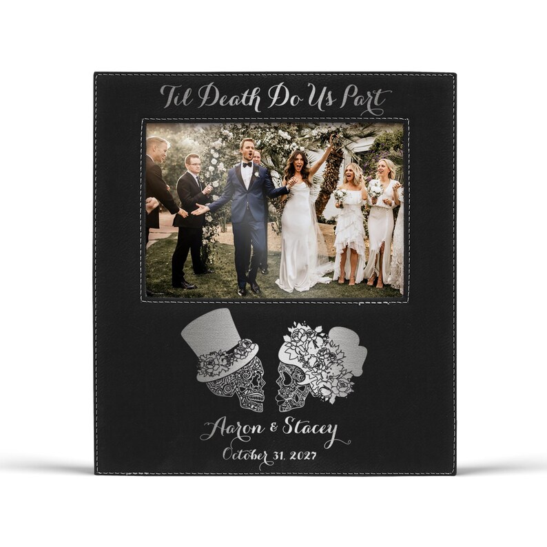 Op de afbeelding: Zwarte fotolijst met een trouwfoto. De lijst heeft bovenaan de tekst "Til Death Do Us Part". Onder de foto staan twee suikerschedelontwerpen en de namen "Aaron & Stacey" met de datum "October 31, 2027".