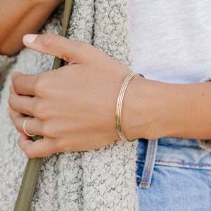 Woman wearing a set of three 14k gold filled bangles and various other Laurel Elaine Jewelry