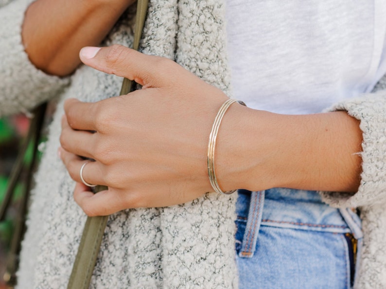 Woman wearing a set of three 14k gold filled bangles and various other Laurel Elaine Jewelry