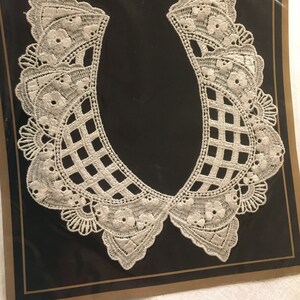 May include: A white lace collar with a floral and geometric design, displayed on a black background. The collar is part of "The Lace Collar Collection". The lace has a delicate, openwork pattern with scalloped edges.