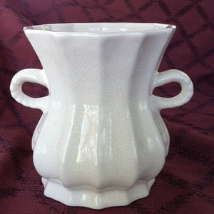 May include: A white ceramic vase with two handles and a crackled glaze. The vase has a rounded body and a flared top.