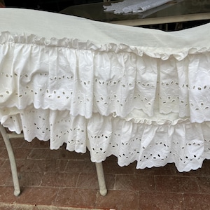 May include: White cotton bed skirt with a ruffled edge and eyelet lace trim. The skirt has two layers of ruffles.