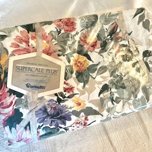 May include: A Wamsutta Supercale Plus full fitted sheet in a white fabric with a floral pattern featuring pink, yellow, and purple flowers with green leaves. The packaging includes a label stating 50% combed cotton, 50% Fortrel polyester, 200 thread count.