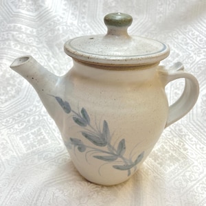 May include: A white ceramic teapot with a green lid and a blue floral design. The teapot has a spout and a handle.