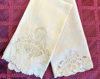 May include: Two white linen tea towels with delicate embroidered floral designs. One towel features a basket of flowers, while the other has a single large flower.
