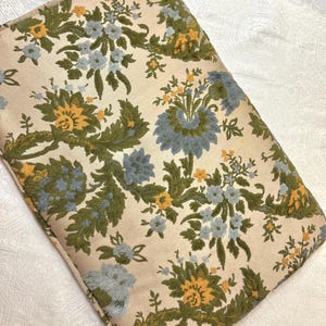 May include: A cream-colored pillow with a floral pattern in shades of green, blue, and yellow. The pillow has a tufted texture and a decorative border.