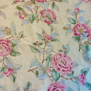 May include: A beige fabric with a floral pattern featuring pink and green flowers. The flowers are a delicate pink with a white center and are surrounded by green leaves.