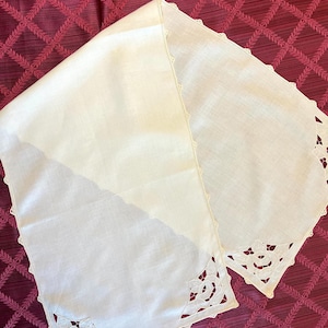 May include: A white linen table runner with delicate lace edging and floral designs. The runner is on a burgundy background.