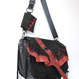 K&ouml;nnte beinhalten: Schwarze Leder-Umh&auml;ngetasche mit roten Akzenten und Spitzenbesatz. Mit einer passenden kleinen Tasche und einem verstellbaren Riemen. Die Tasche hat einen Schnallenverschluss und dekorative Quasten.