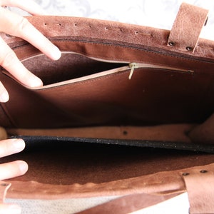 May include: A brown leather tote bag with a textured exterior, featuring a spacious interior compartment, a zippered pocket along the inner wall, and a removable black felt insert at the base. The bag is constructed with visible stitching.