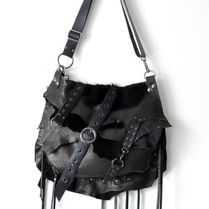May include: Black leather shoulder bag with a unique, layered design. Features a long adjustable strap, metal hardware, and decorative fringe. The bag has a distinctive, edgy aesthetic.